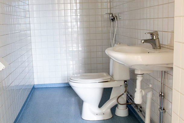 Badrum med vitt kakel på väggar och blå våtrumsmatta på golvet. Färger och material varierar mellan lägenheterna
