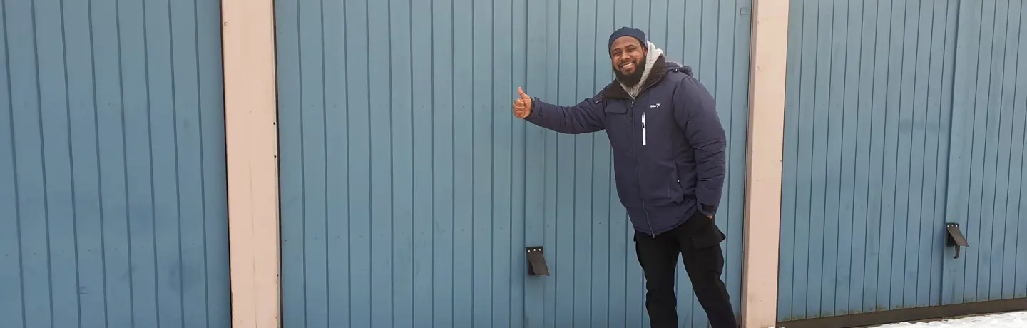 Mohammed på Eidar ger tummen upp utanför en garageport