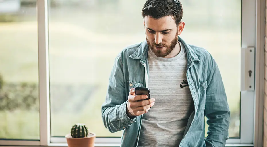 Man i fönster står och tittar i telefonen