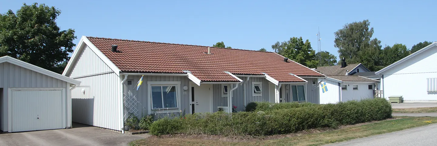 Enplans radhus i Åsaka med uteplats med omgivande häck och med ett garage vid sidan om.