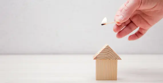 litet trähus med en hand med tändsticka bredvid