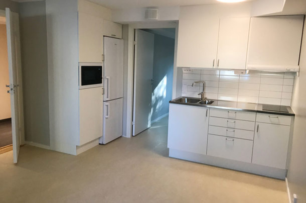 An apartment with white painted walls, bright lninoleum floor and a kitchenette