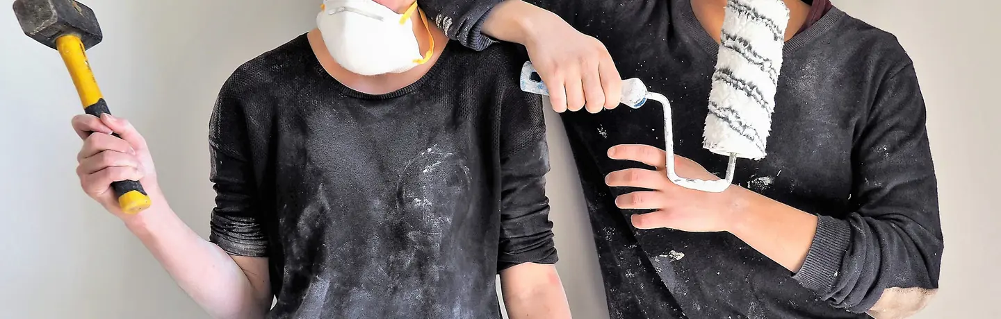 Ett par med målarroller och hammare, det syns att de fixat hemma då de har målarstänk på kläderna
