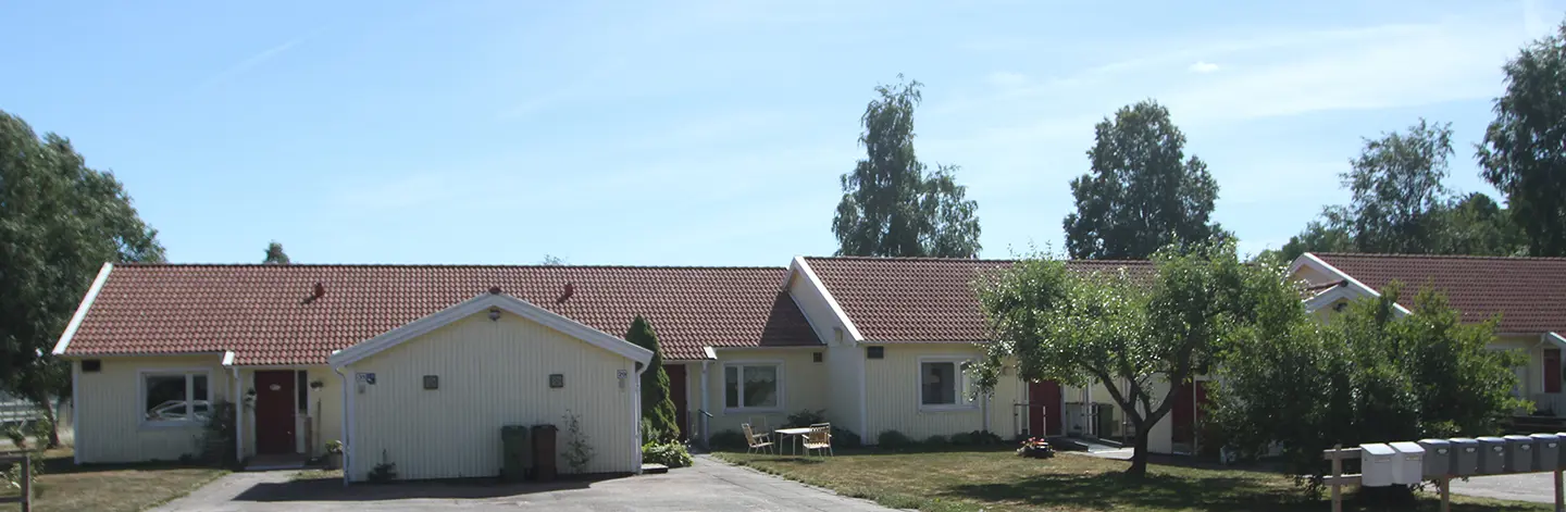 Radhus på Kyrkväktarnas väg och Västra Lindåsvägen i Upphärad. Ljust gula fasader, röda dörrar och gräsmattor och träd i förgrunden