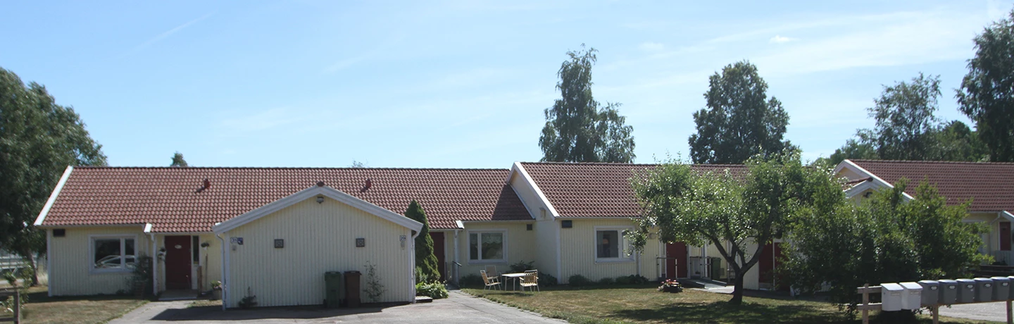 Radhus på Kyrkväktarnas väg och Västra Lindåsvägen i Upphärad. Ljust gula fasader, röda dörrar och gräsmattor och träd i förgrunden
