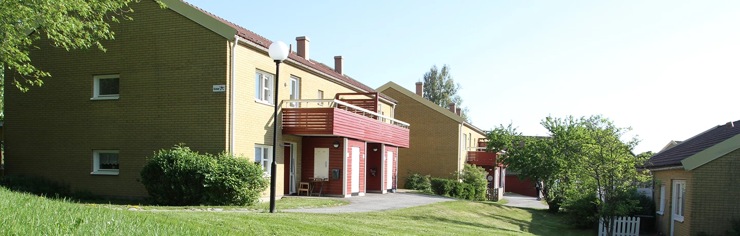 Fasadbild över kvarteret Källstorp i Trollhättan. Tvåvåningshus i tegel med röda balkonger och uteförråd. Gräsmattor och träd mellan husen.
